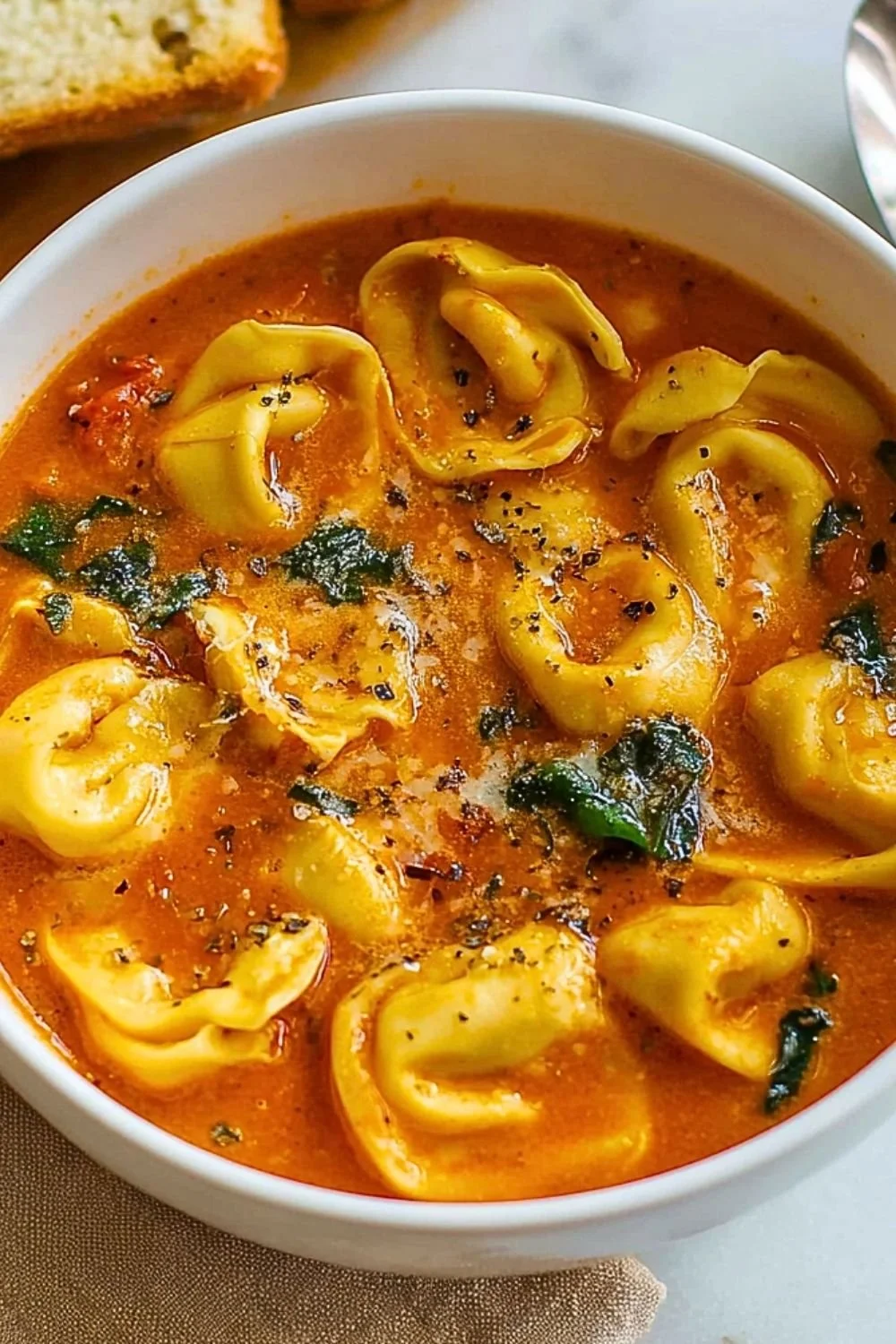Bowl of cozy tomato tortellini soup topped with basil and cheese