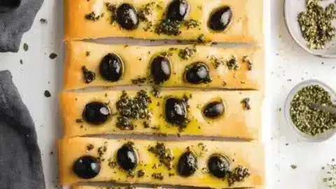 Homemade focaccia topped with herbs and olives, showcasing a delicious DIY recipe.