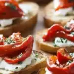 Roasted red peppers goat cheese crostini served on a platter with herbs.