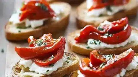 Roasted red peppers goat cheese crostini served on a platter with herbs.
