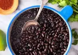 Bowl of cooked black beans on a wooden table garnished with herbs.