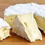 Delicious and creamy Brie cheese served on a wooden board with fruits and nuts.