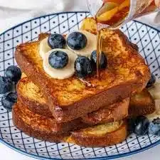 Plate of golden brown Brioche French Toast topped with berries and syrup