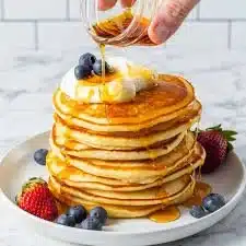 Stack of fluffy pancakes topped with syrup and berries