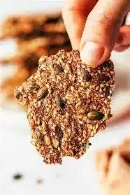 Homemade 4-ingredient seed crackers displayed on a wooden board with seeds around.