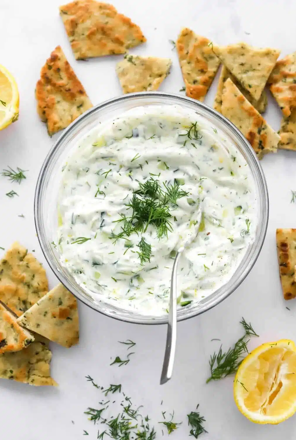 Bowl of easy healthy tzatziki sauce with fresh ingredients on a wooden table.