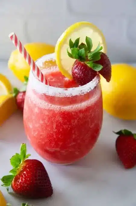 Delicious frozen strawberry lemonade in a glass with fresh strawberries and lemon slices.