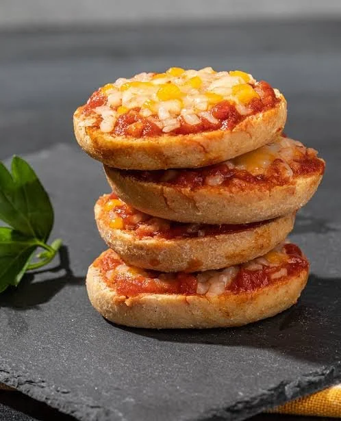 Mini pizza bagels topped with cheese and pepperoni on a baking tray.
