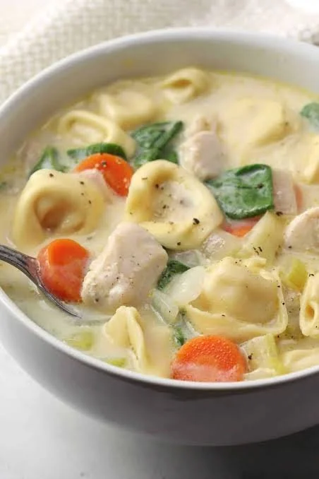 Bowl of creamy chicken tortellini soup garnished with fresh herbs and vegetables
