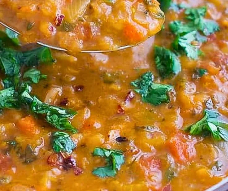 Bowl of easy spicy tomato lentil soup garnished with herbs