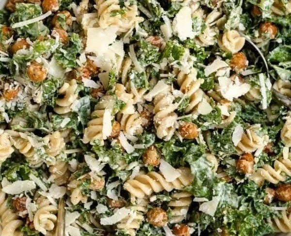 Kale Caesar Pasta Salad topped with croutons and parmesan cheese in a bowl.